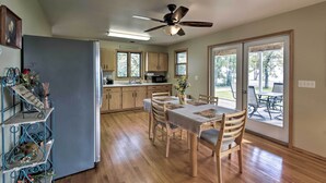 A spacious kitchen with wooden cabinets, a dining table with chairs, a ceiling fan, and large windows.