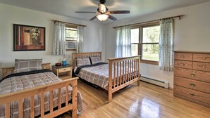 A bedroom with two wooden beds, a ceiling fan, a nightstand, a dresser, and a window with curtains.