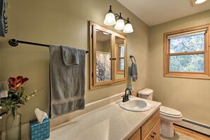 A bathroom with a sink, mirror, towel rack, toilet, and window.