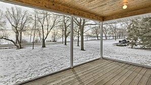 A covered wooden deck with a view of a snowy landscape and trees.