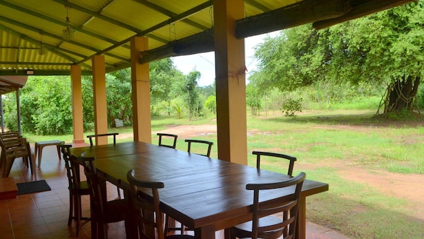 An outdoor covered dining area with a long wooden table and chairs, surrounded by greenery. - Wilpattu Dilsara Holiday Resort (Pahala Maragahawewa)