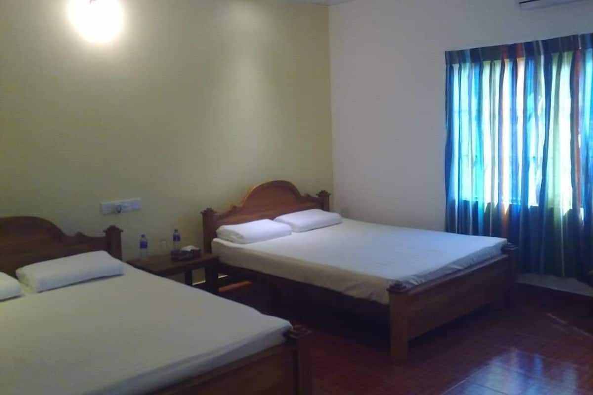 Ein Hotelzimmer mit zwei Einzelbetten, einem hölzernen Kopfteil, einem Nachttisch mit einer Flasche und einem Fenster mit Vorhängen.