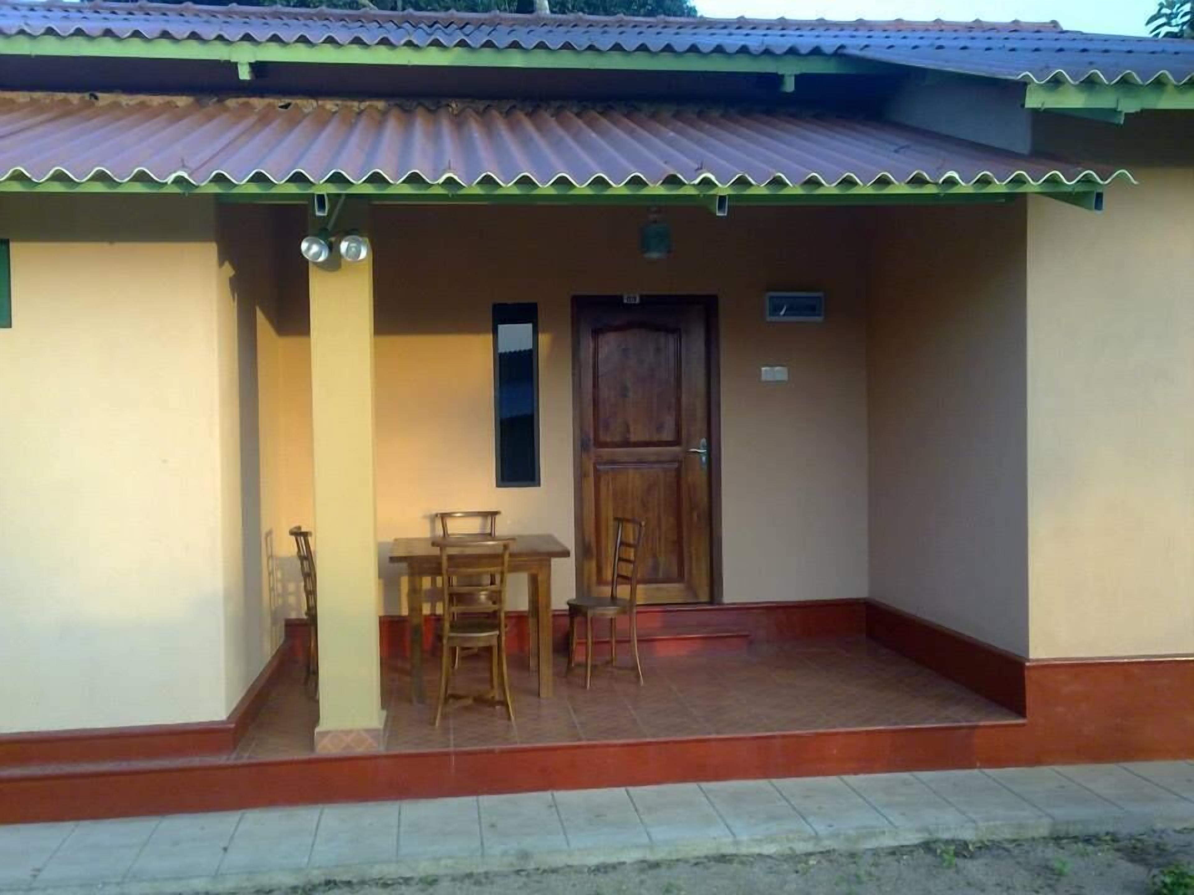 Un edificio con un porche de baldosas, una puerta de madera y dos sillas.