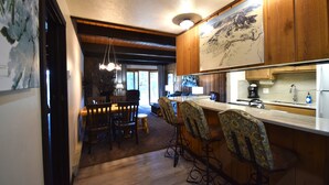 A modern kitchen with wooden cabinets, a bar area with patterned stools, and a large framed picture on the wall. - Great Location=Great Vacation. Dog Friendly Condo w/ Awesome Ski Access (Mt. Crested Butte)