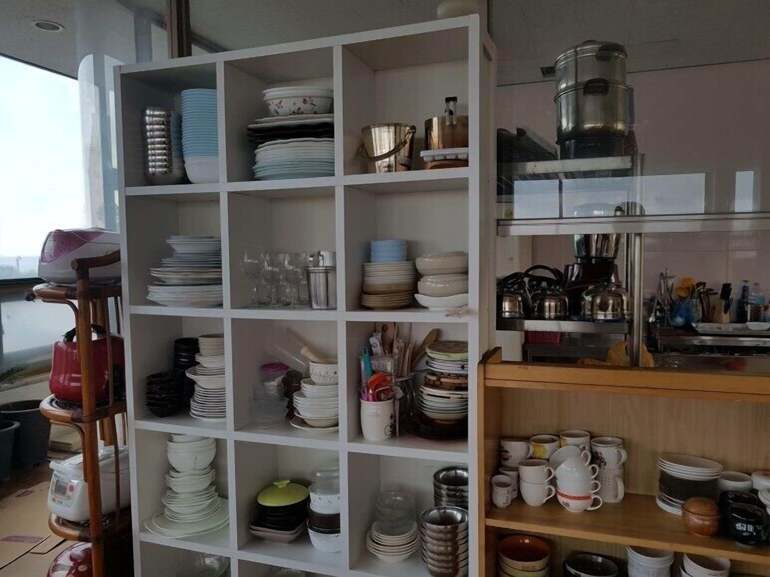 A kitchen with white shelving units filled with plates, bowls, and mugs.