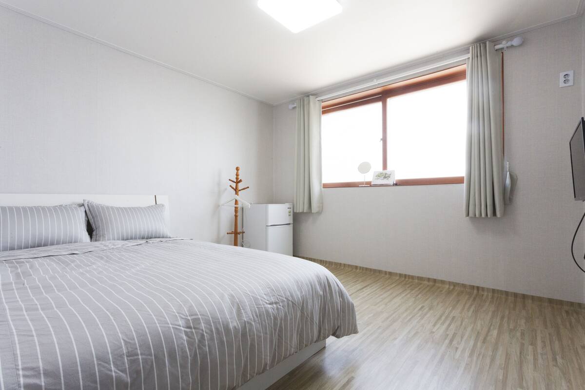 A bedroom with a bed, a window with curtains, a bedside table, and a wall-mounted TV.
