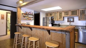 A kitchen with wooden bar stools, a stainless steel refrigerator, and wooden cabinets. - Close to Everything! Ski-In/Out Condo. Doggie Friendly, Mtn Views, Fireplace (Mt. Crested Butte)