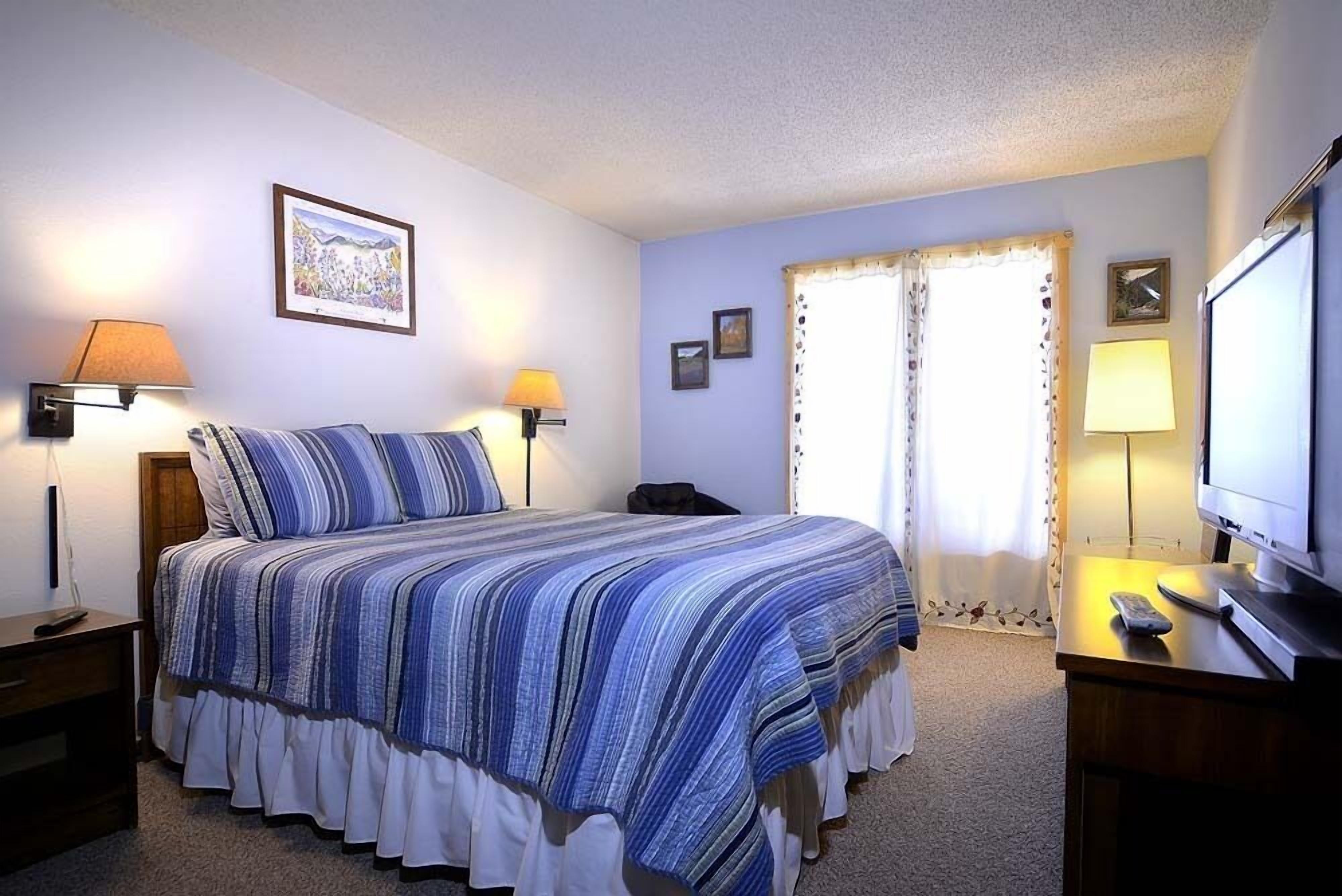 A bedroom with a bed, two bedside lamps, a television, and a framed picture on the wall.