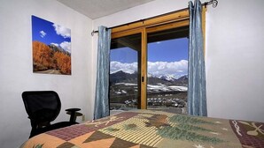 A hotel room with a large window offering a mountain view, a bed with a patterned bedspread, a chair, and a small table. - Close to Everything! Ski-In/Out Condo. Doggie Friendly, Mtn Views, Fireplace (Mt. Crested Butte)