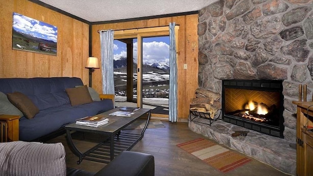 A cozy living room with a stone fireplace, a blue sofa, and a view of mountains through a glass door. - Close to Everything! Ski-In/Out Condo. Doggie Friendly, Mtn Views, Fireplace (Mt. Crested Butte)