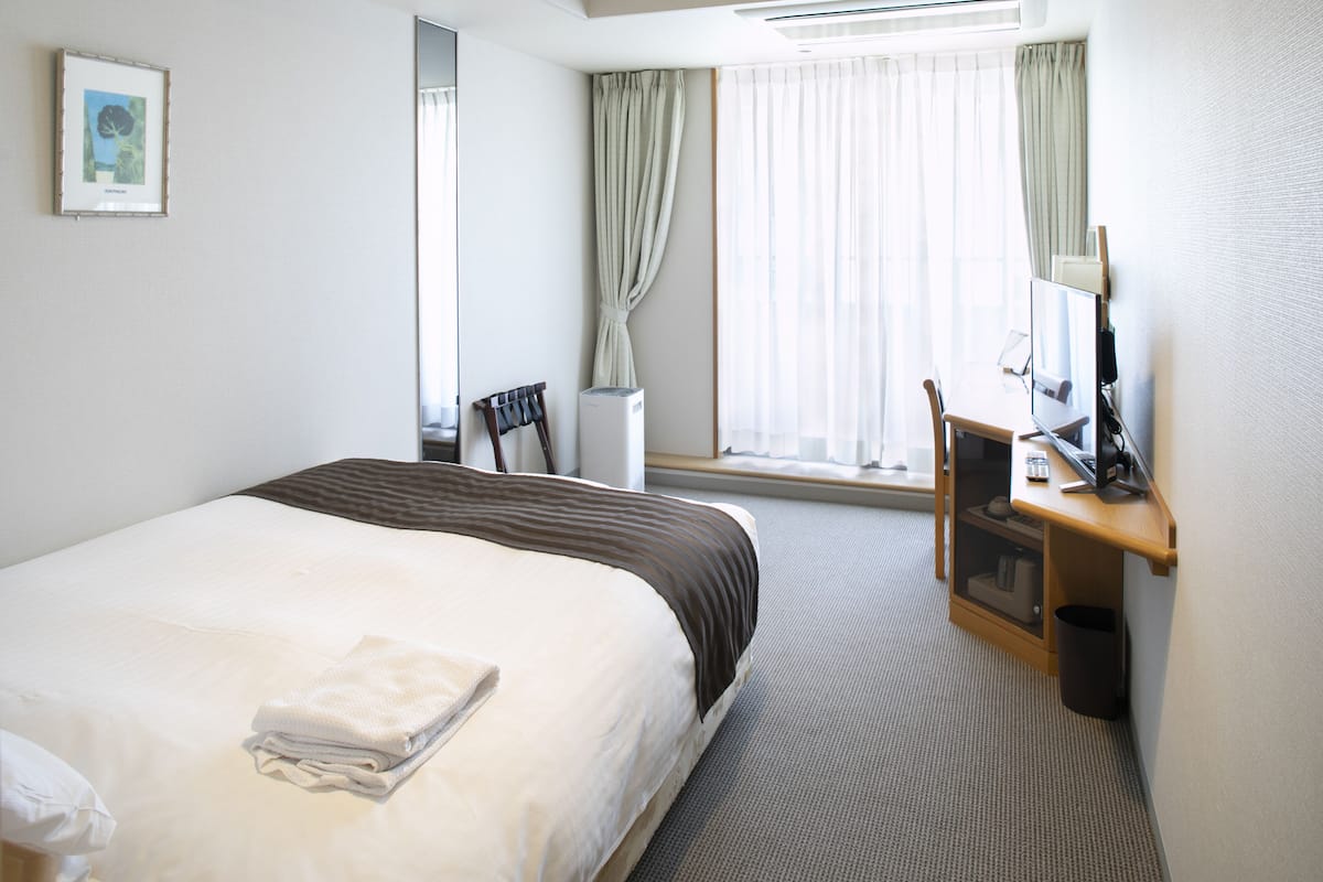 A hotel room with a bed, a desk, a chair, a TV, and a window with curtains.