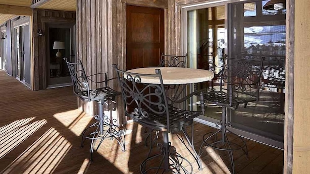 A wooden deck with a round table and chairs, a door, and a window with a view. - Spacious Mountain Condo Retreat! Ski-In/Out w/ Views, Fireplace, Dog Friendly (Mt. Crested Butte)