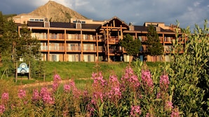 A multi-story lodge with balconies, a mountain backdrop, and a sign indicating a ski resort. - Spacious Mountain Condo Retreat! Ski-In/Out w/ Views, Fireplace, Dog Friendly (Mt. Crested Butte)