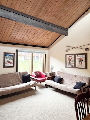 A room with a wooden ceiling, two sofas, a red chair, a small table with a lamp, and framed pictures on the wall. - Spacious Mountain Condo Retreat! Ski-In/Out w/ Views, Fireplace, Dog Friendly (Mt. Crested Butte)
