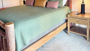 A bed with a green quilt, wooden headboard, and multiple pillows. There are two bedside tables with lamps and a small drawer. - Spacious Mountain Condo Retreat! Ski-In/Out w/ Views, Fireplace, Dog Friendly (Mt. Crested Butte)