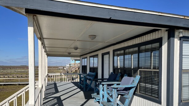 A covered outdoor area with a wooden deck, blue chairs, and a view of a distant building.
