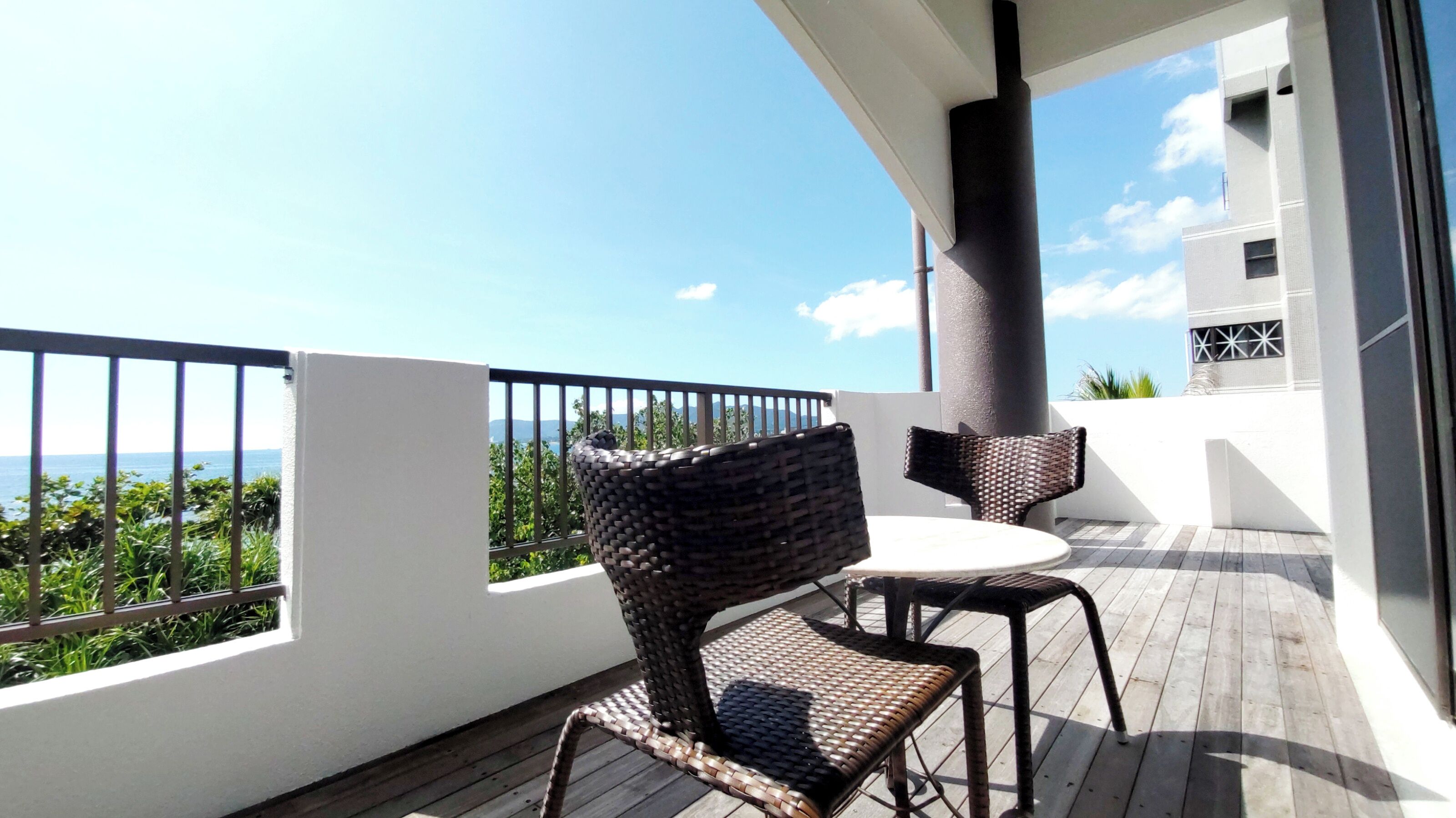 Un balcon agrémenté de meubles en osier, d’une table blanche et offrant une vue sur la mer.