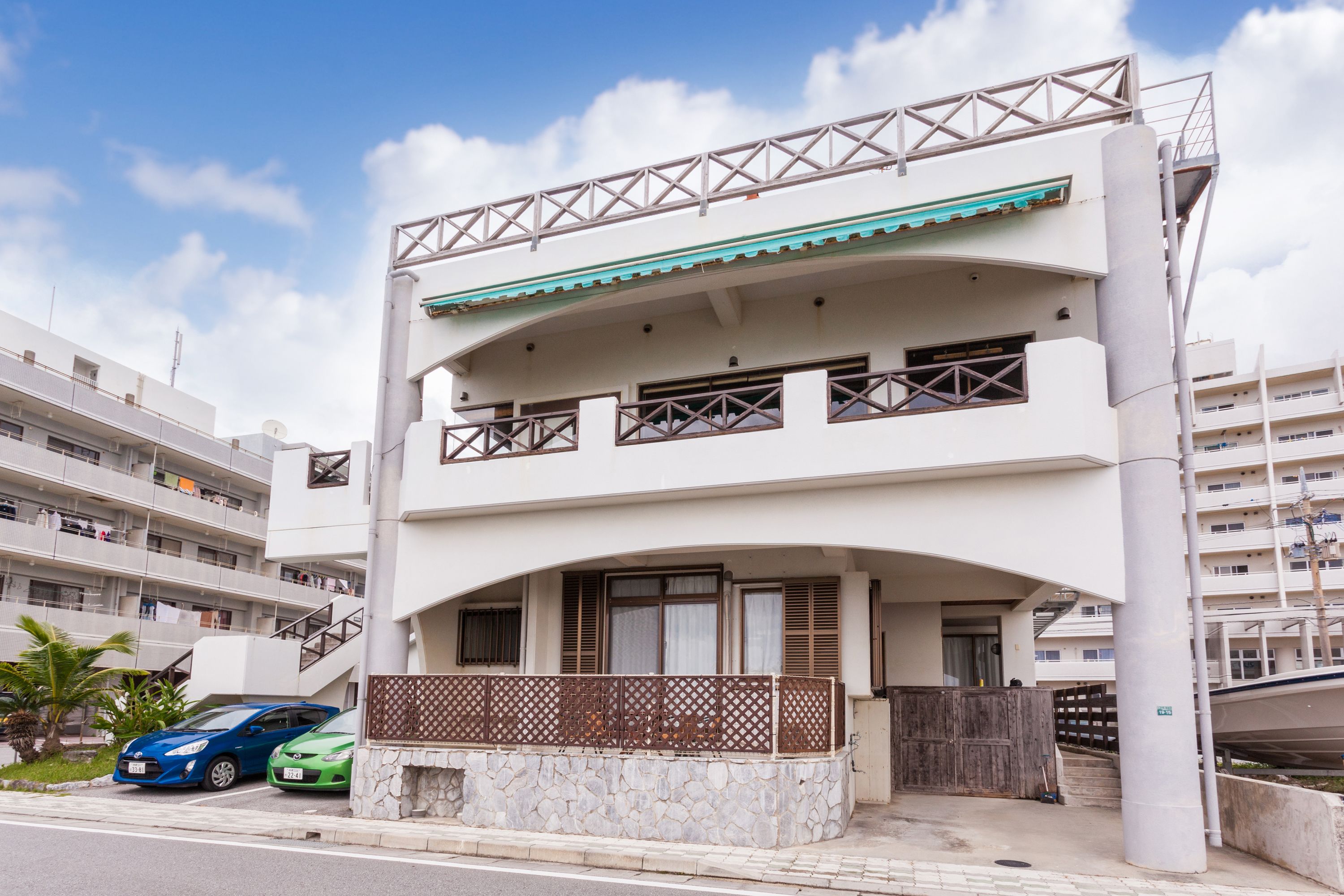 A multi-story residential building with a balcony, a stone base, and a staircase leading to the upper floor.
