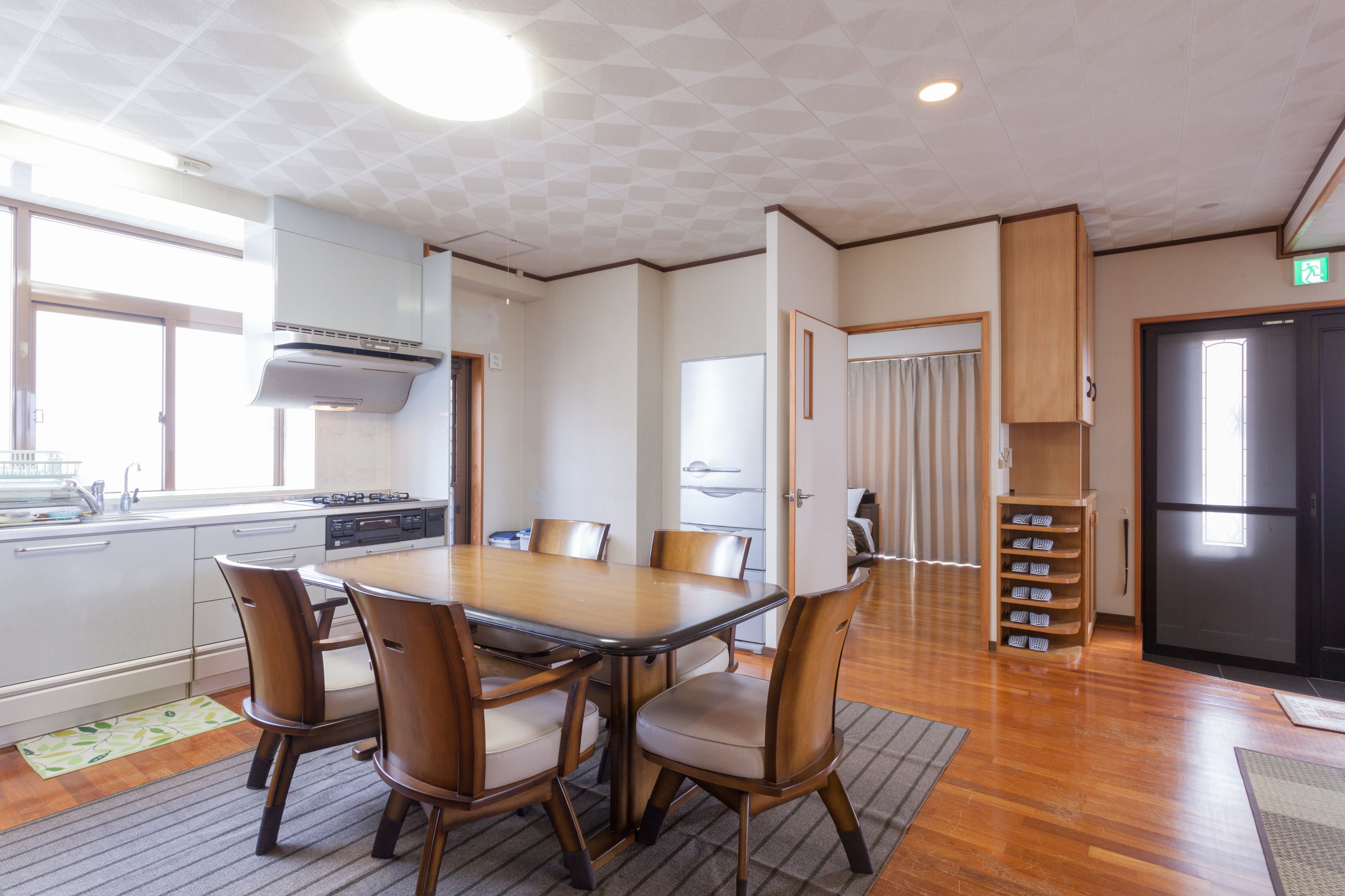 A modern kitchen with a dining area, featuring a wooden table and chairs, a built-in oven, and a refrigerator.