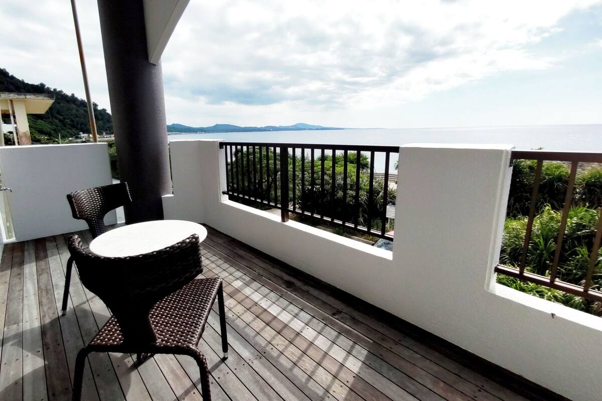 Un balcón con mesa y sillas, vista al mar y barandilla.