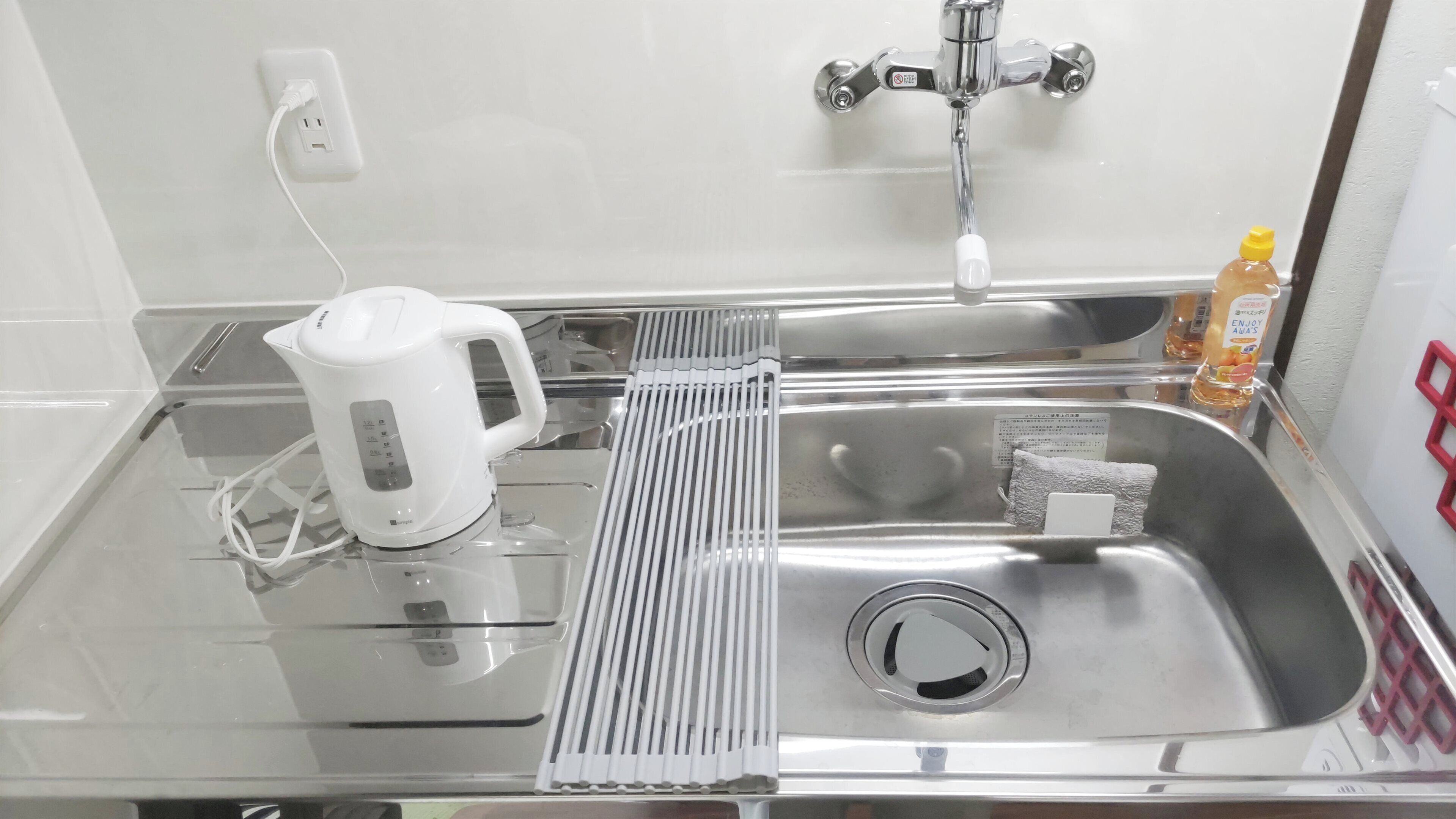 A modern kitchen with a stainless steel sink, a kettle, and a bottle of orange juice.