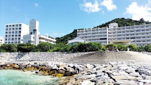 Un hotel a la costa amb múltiples plantes, una escala de pedra que porta a la platja, i vista al mar.