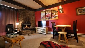 Una sala de estar acogedora con chimenea de piedra, televisión y una pared roja con un cuadro de un pez.