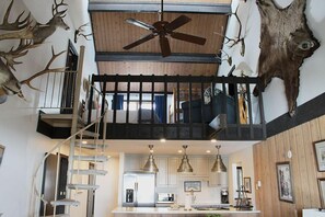 Experience the open-plan living area with a central kitchen island and spiral staircase leading to an upper level with a mounted deer head.