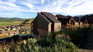 A modern building with a sloped roof, surrounded by lush greenery and a distant village. - Ideal Mountain Condo! Ski-In/Ski-Out, Slopeside with Beautiful Views (Mt. Crested Butte)