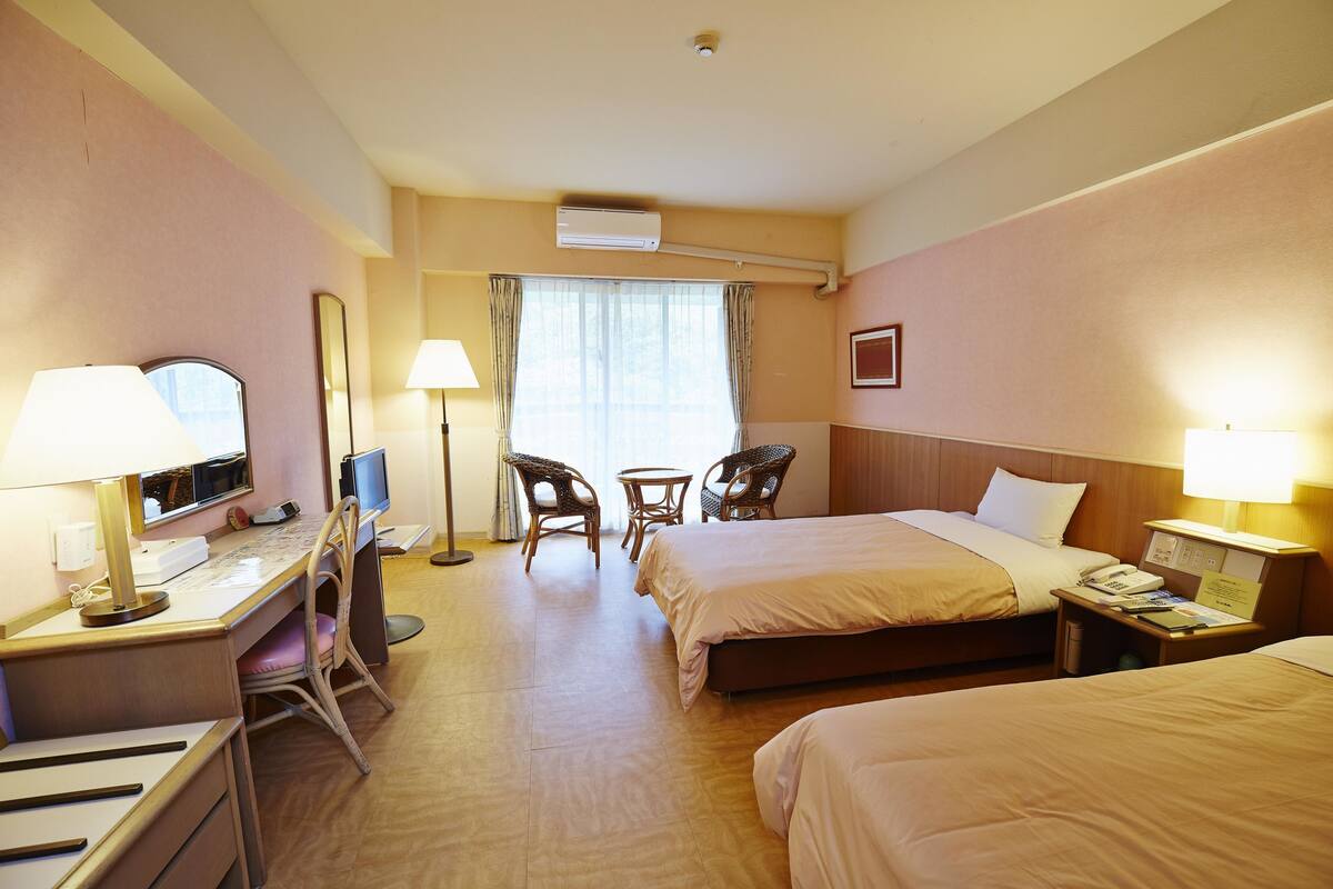 Une chambre d’hôtel avec deux lits, un bureau avec un ordinateur, une chaise, une petite table et une lampe.