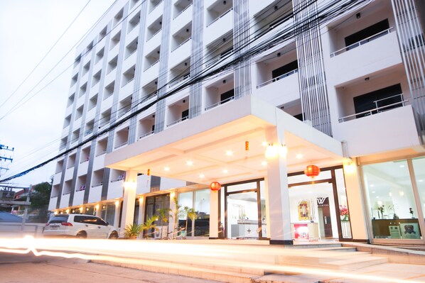 Um hotel moderno com entrada coberta, vários andares e um carro estacionado na frente.