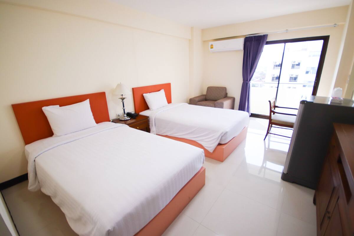 A hotel room with two beds, a desk, a chair, and a window with curtains.