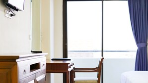 Habitación de hotel con un escritorio de madera, una silla, una cama, un televisor montado en la pared y un ventanal con cortinas.