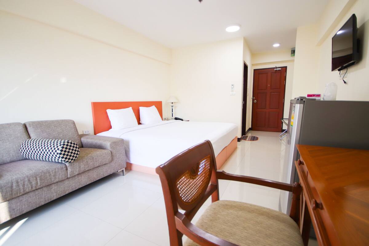 A hotel room with a bed, a sofa, a wooden chair, a desk, and a television.