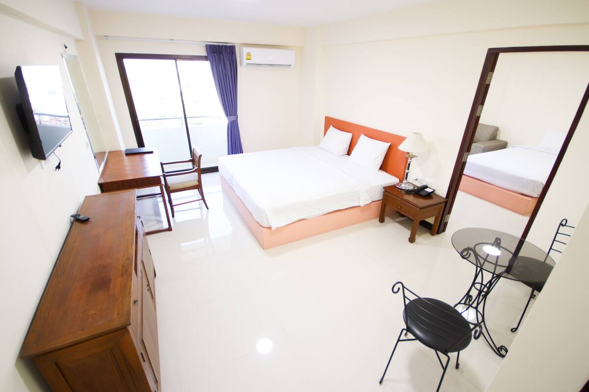 A hotel room with a bed, a desk, a chair, a small table, a TV, and a window with curtains.