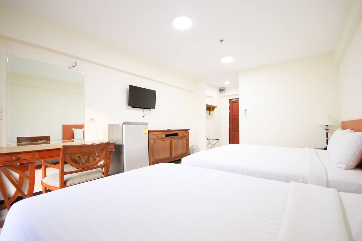 A hotel room with two beds, a desk with a chair, a television, and a refrigerator.