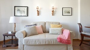A living room with a beige sofa, a small table with a lamp, and two wall-mounted light fixtures. - SEVEN GUEST HOUSE, a departing point to visit Lisbon and Sintra (Casal de São Brás)
