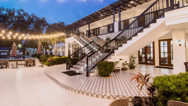 A spacious outdoor patio with a staircase leading to an upper level, surrounded by potted plants and outdoor furniture. - The Mansion (Mabalacat City)