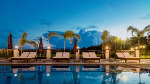 A poolside area with lounge chairs and umbrellas, surrounded by palm trees and a clear sky. - The Mansion (Mabalacat City)