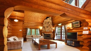 A log cabin interior with a stone fireplace, wooden furniture, and large windows. - Urube Village (Tsumagoi)