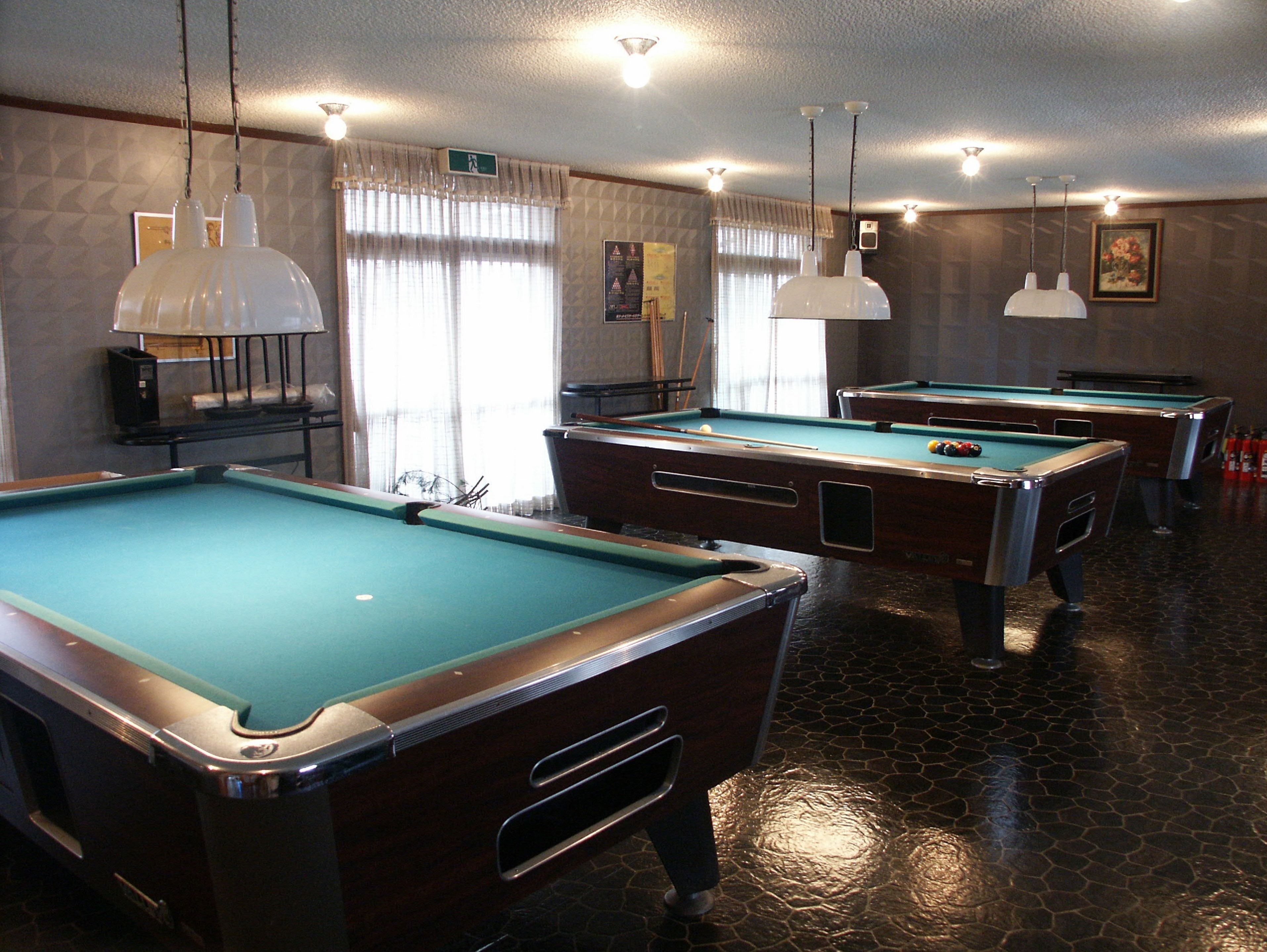 A pool hall with multiple pool tables, overhead lighting, and a patterned floor.