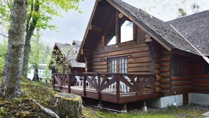 A log cabin with a wooden deck and chairs, surrounded by trees. - Urube Village (Tsumagoi)