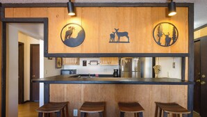 Une cuisine avec des tabourets de bar en bois, un îlot central et un mur orné de silhouettes d’animaux.