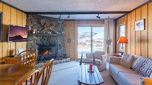Un salon chaleureux avec une cheminée en pierre, des murs en bois, un coin repas et un canapé.