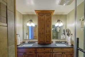 Een badkamer met twee wasbakken, houten kastjes, een grote spiegel en wandlampen.