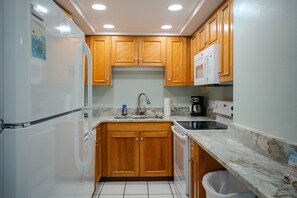 A compact kitchen with wooden cabinets, a built-in microwave, a coffee maker, and a dishwasher.