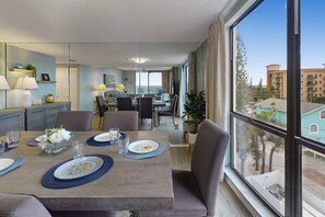 Habitación de hotel con comedor, sala de estar y un amplio ventanal con vistas a edificios.