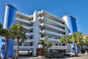Ein mehrstöckiges Hotel im modernen Stil, mit Balkonen und einem Parkplatz mit Autos.