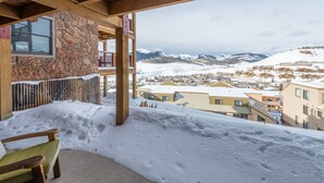 Ein mit Schnee bedeckter Balkon mit Steinmauer, Holzboden und Blick auf eine verschneite Stadt und Berge.