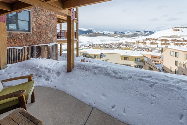 A snow-covered balcony with a stone wall, wooden deck, and a view of a snow-covered town and mountains. - Great location! Ski-In/Out Dog Friendly Condo w/ Fireplace & Views (Mt. Crested Butte)